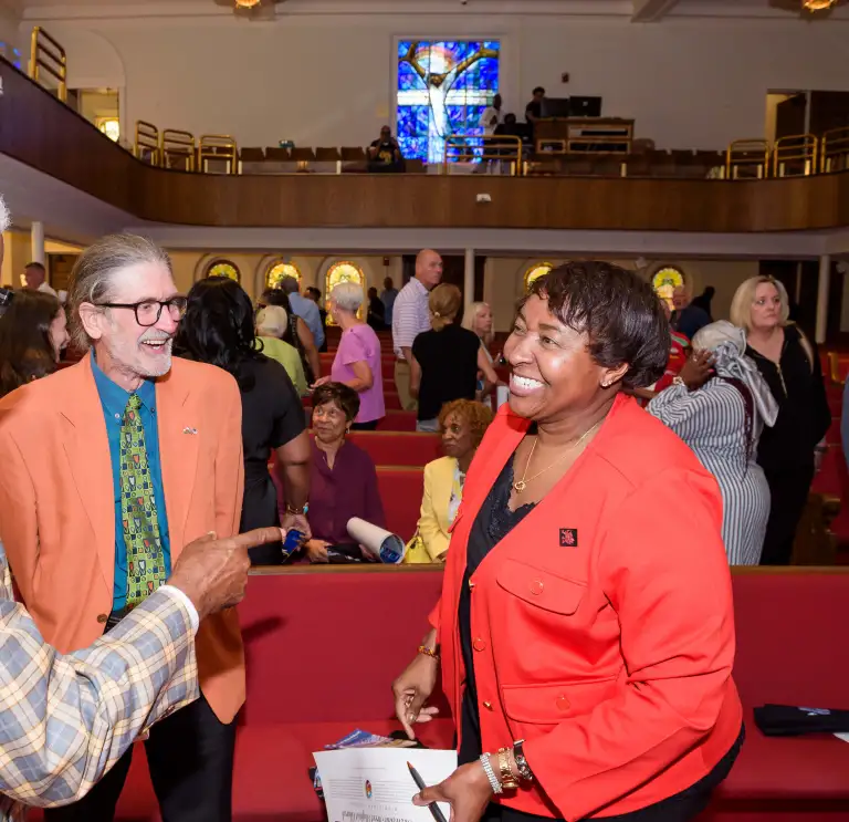 Three people smiling and talking inside the church with the stained glass window in the background.