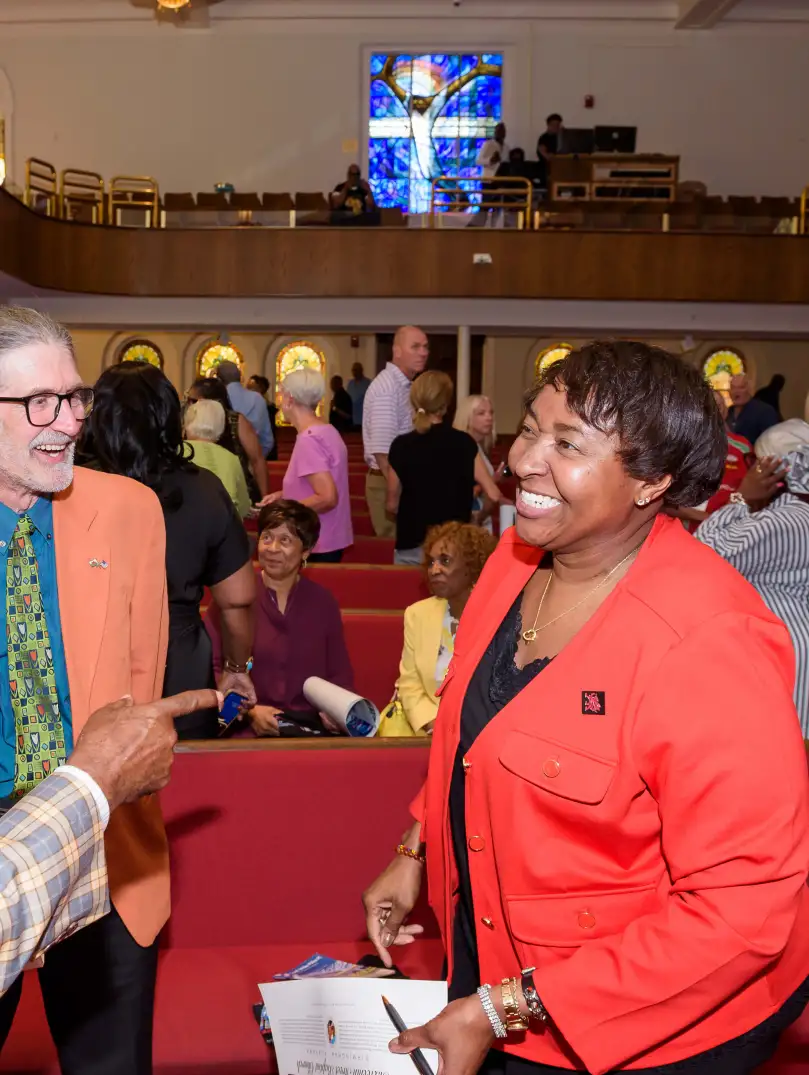 Three people smiling and talking inside the church with the stained glass window in the background.