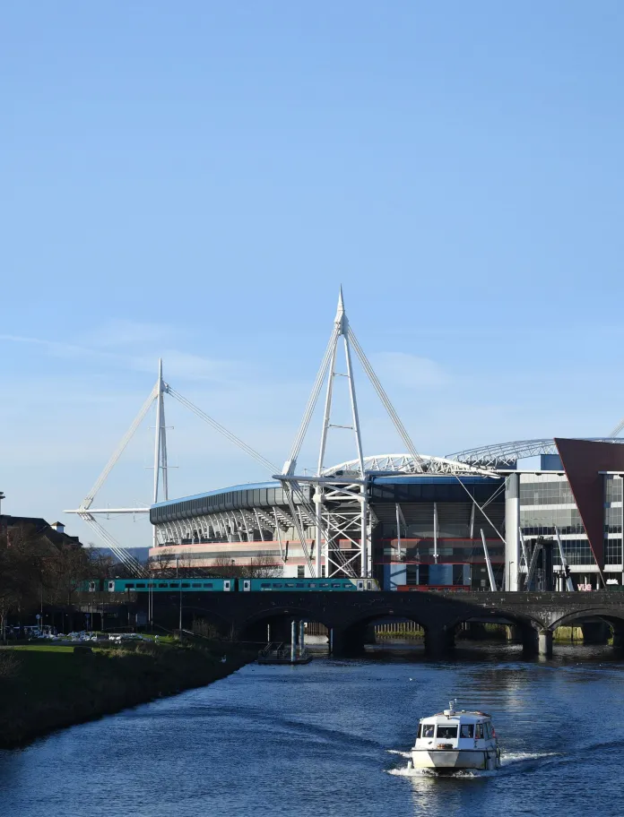 A river with a boat and a large sports stadium behind.