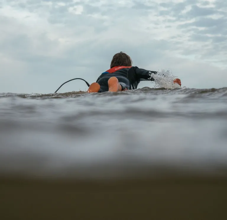 A person lying on a surf board in the sea.