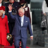 King Charles III accompanied by the Queen Consort, walking down some stairs and waving at crowds