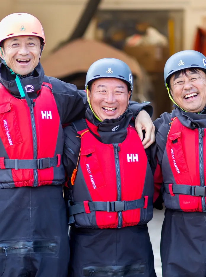 Three male Japanese fire brigade members stood next to each other smiling in sea rescue clothing at UWC Atlantic College
