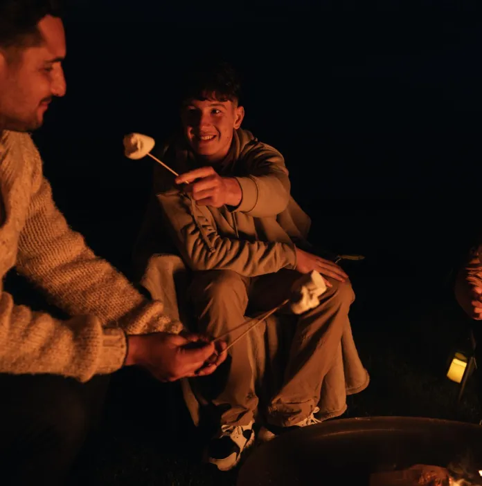 People sat around a campfire eating toasted marshmallows.