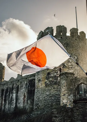 La bandera japonesa ondeando en un día soleado frente a la majestuosa vista histórica del castillo de Conwy en Gales, hermanado con el castillo de Himeji en Japón.