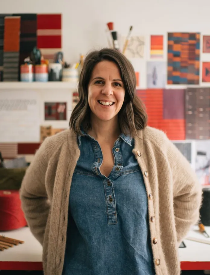 La artista textil galesa Llío James de pie junto a su escritorio en su estudio.