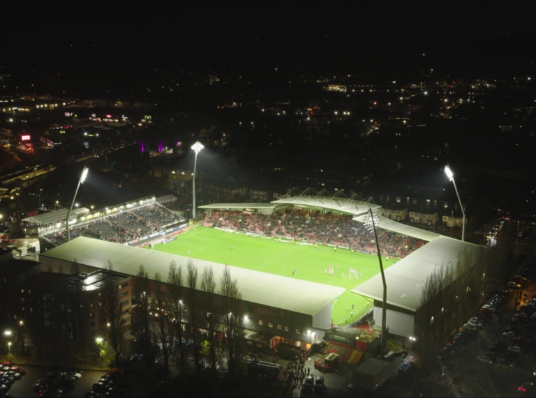 Vue aérienne du stade de football de Wrexham AFC la nuit, avec les projecteurs illuminant le terrain et un match en cours