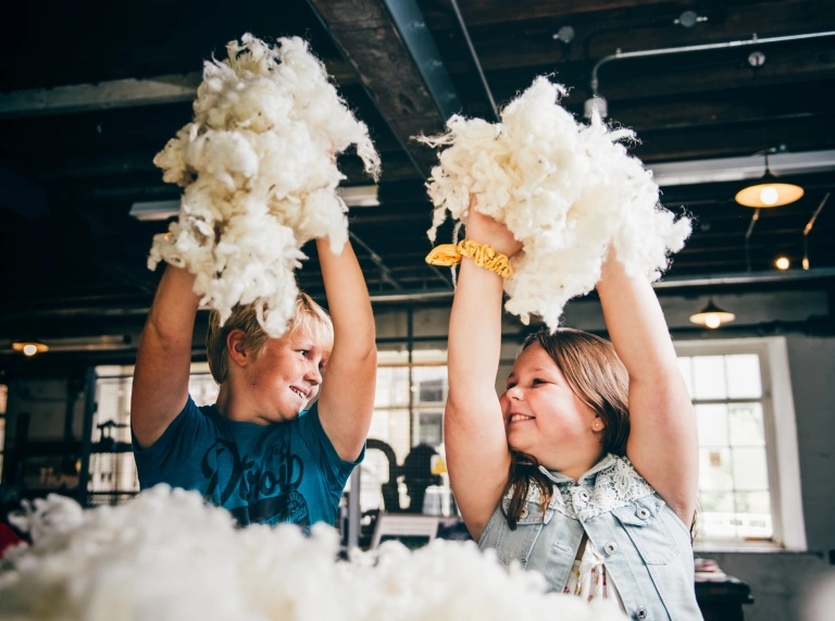 Two children smiling to each other and holding wool in the air.