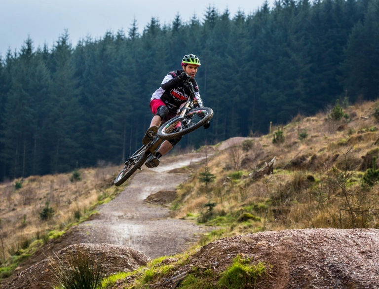 Ein Mountainbiker nimmt einen großen Sprung in einem bewaldeten Mountainbike-Park
