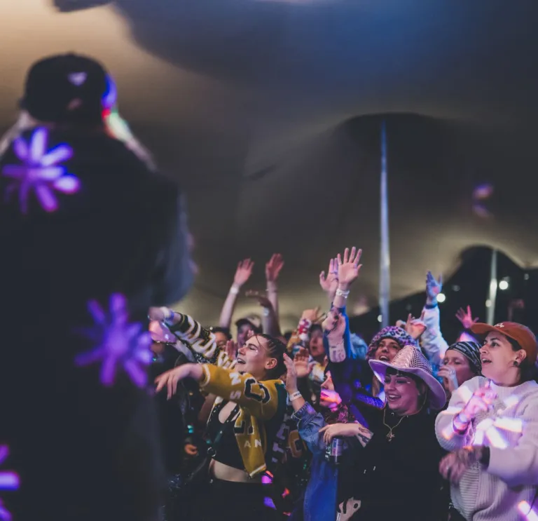 A crowd of people at a festival dancing and singing while looking up at a stage
