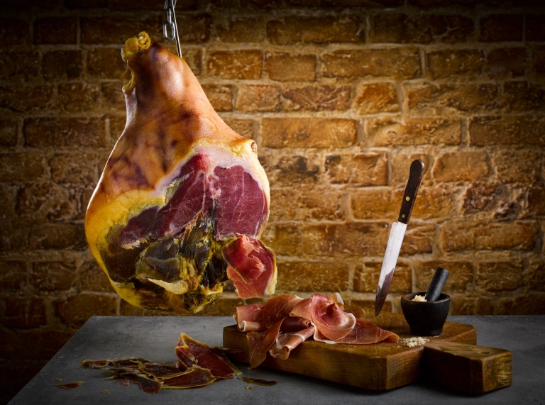 Jamón colgando de un gancho y un cuchillo junto al jamón rebanado.