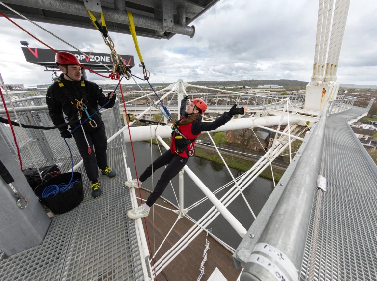 Two people standing on the top of a building in harnesses.