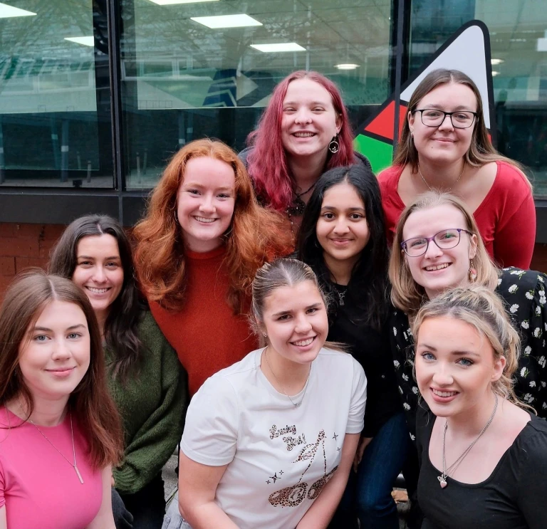 9 young women crouched in front of Urdd logo