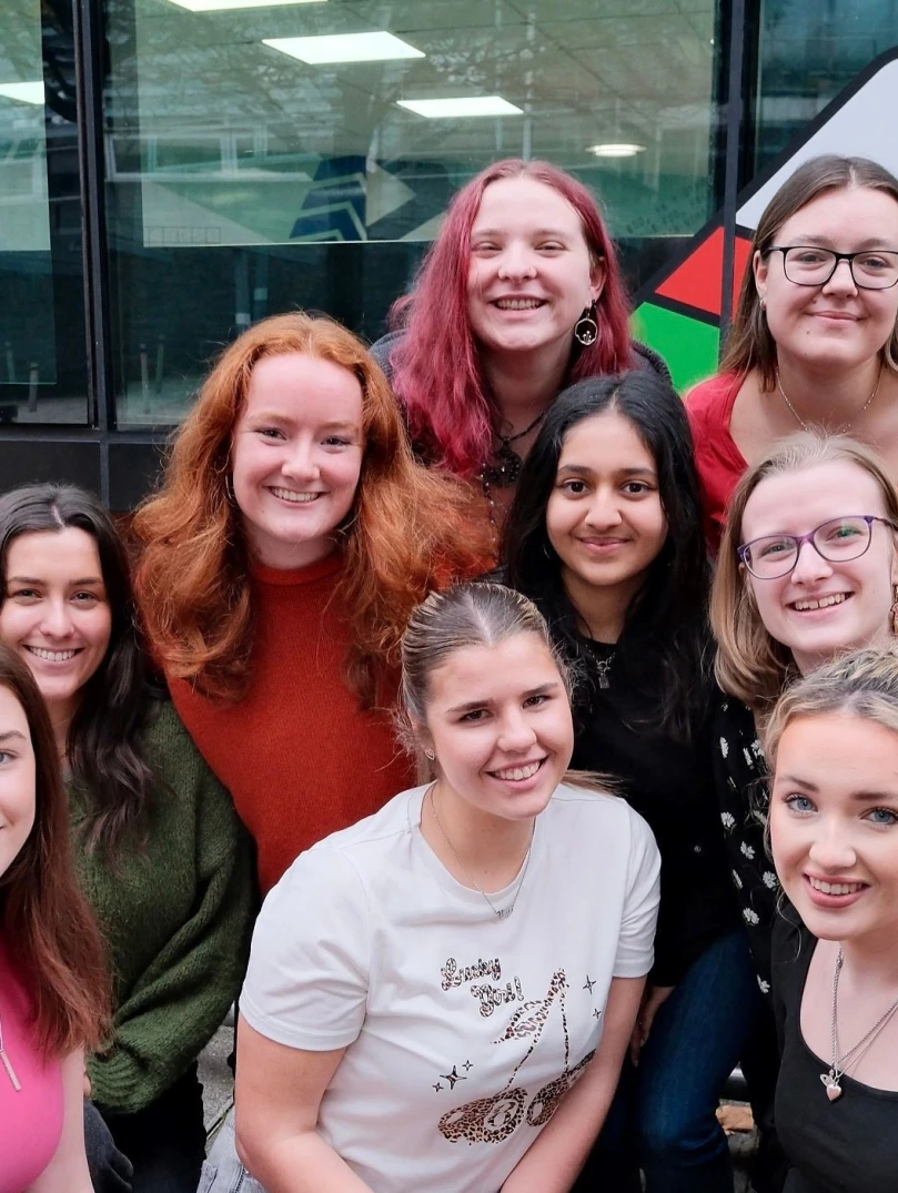 9 young women crouched in front of Urdd logo