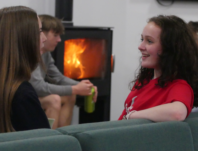 Des personnes discutent sur un canapé avec un poêle à bois en arrière-plan.
