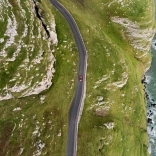 An aerial shot of a car driving along a mountainous coastal road 