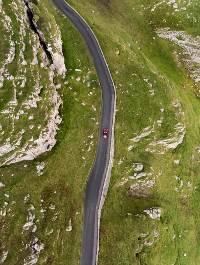 An aerial shot of a car driving along a mountainous coastal road 