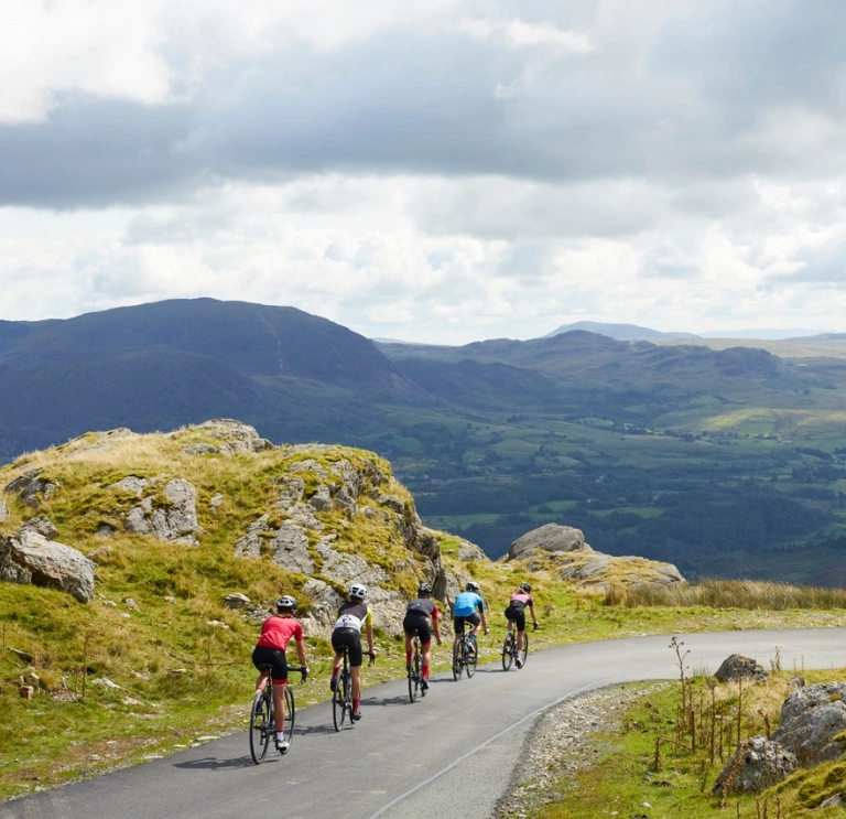 Five people on road bikes cycling down a scenic road against the backdrop of mountains