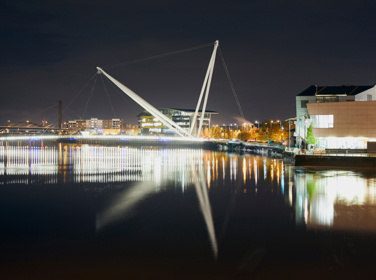 nighttime photo of footbridge with lights from building reflecting in river