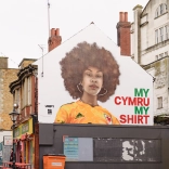 A huge mural of a woman wearing a yellow football shirt, on the side of a building.