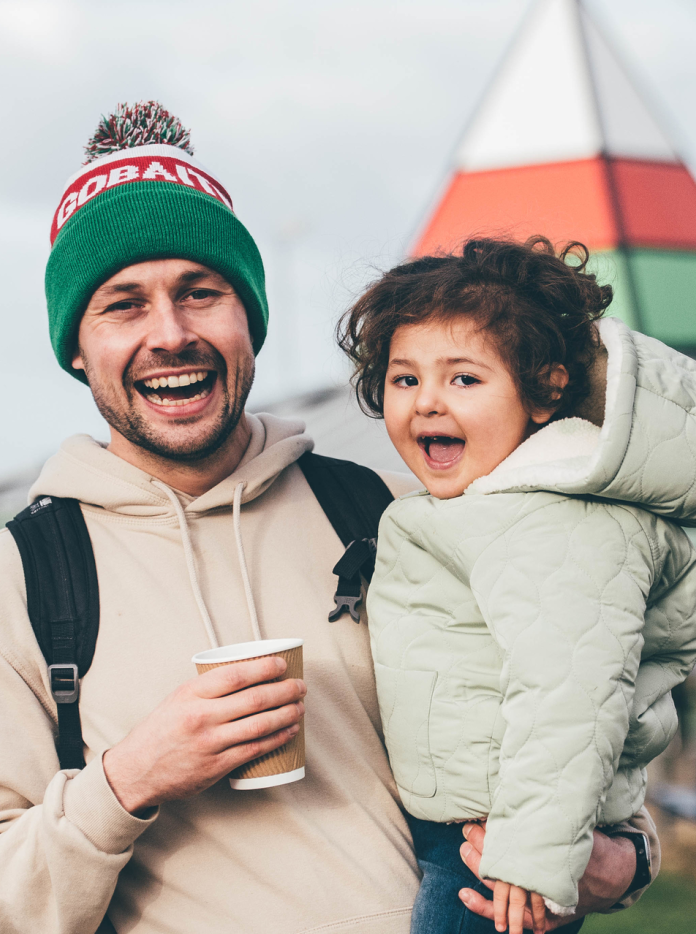 Un homme tient un petit enfant dans les bras, tous deux souriants.