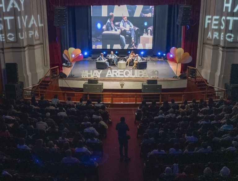 Four speakers on stage in front of an audience.