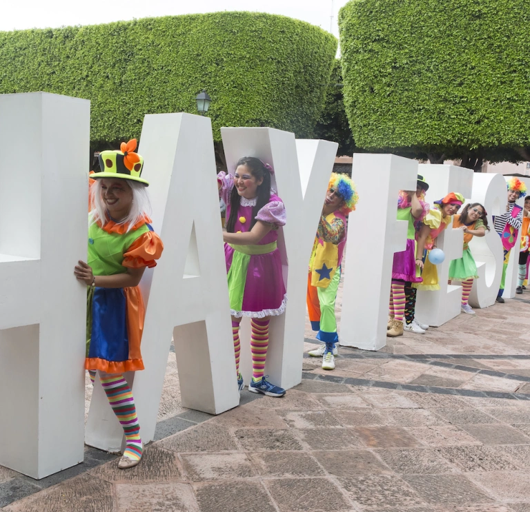 Colourfully dressed people amongst large Hay Festival letters.