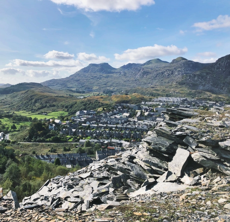 Una montaña de pizarra en primer plano, con casas adosadas y más montañas en el fondo