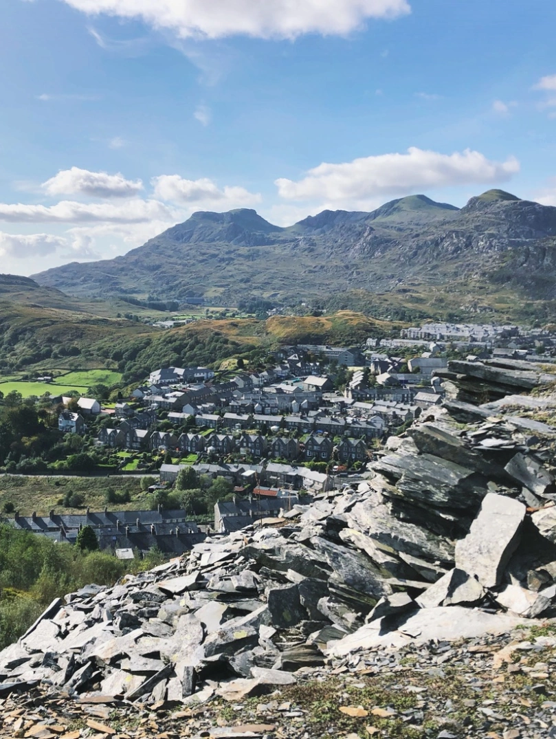 A mountain of slate in the foreground, with terraced houses and further mountains in the background