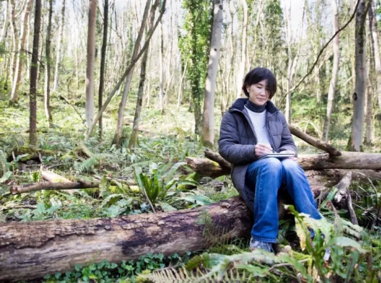 Mari Wirth sitting on a log in a forest.