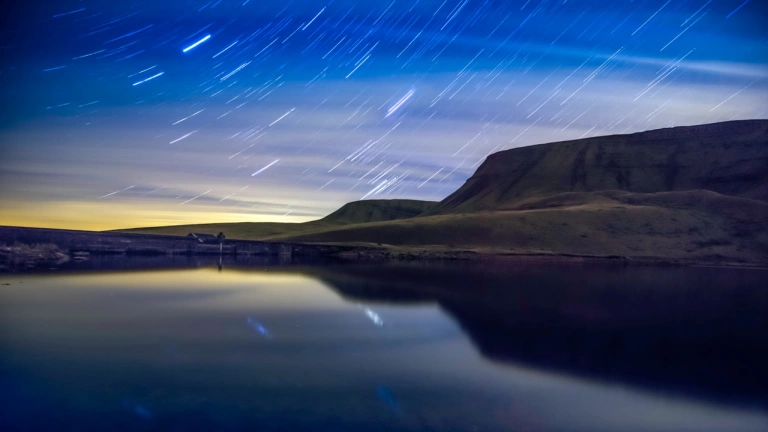 A night shot of a lake and some mountains with starry skies behind