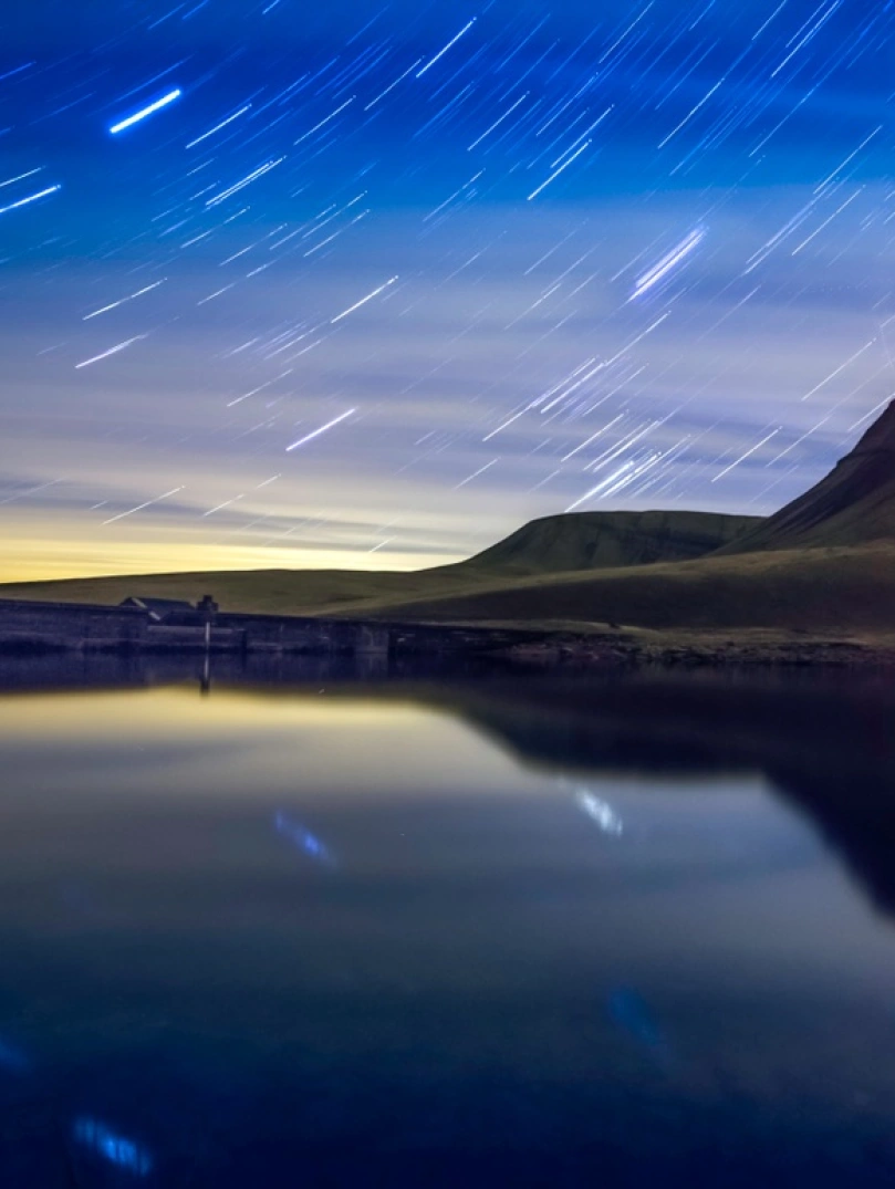 A night shot of a lake and some mountains with starry skies behind