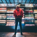 A young boy looking up at a colourful cabinet full of Welsh blankets.