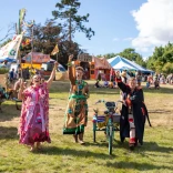 Three people dressed in bright festival costumes raising their arms to wave 
