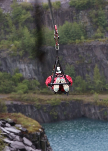 A person in a harness flying down a zip wire against a mountainous background