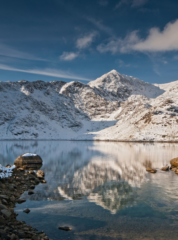 Walker looking towards snow-covered summit of  Yr Wyddfa (Snowdon)from Llyn Llydaw lake, Snowdonia