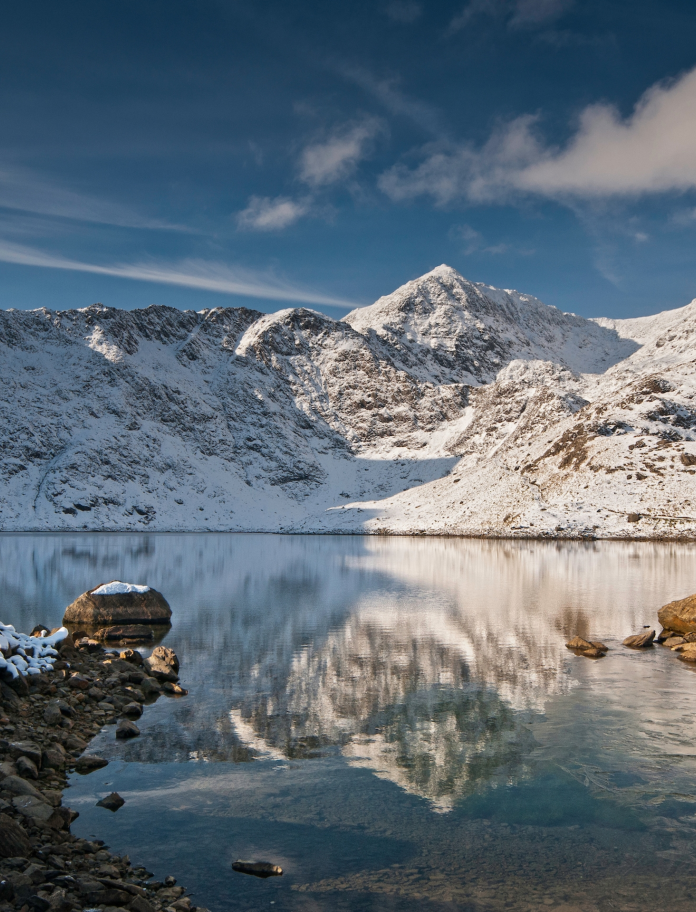 Walker looking towards snow-covered summit of  Yr Wyddfa (Snowdon)from Llyn Llydaw lake, Snowdonia