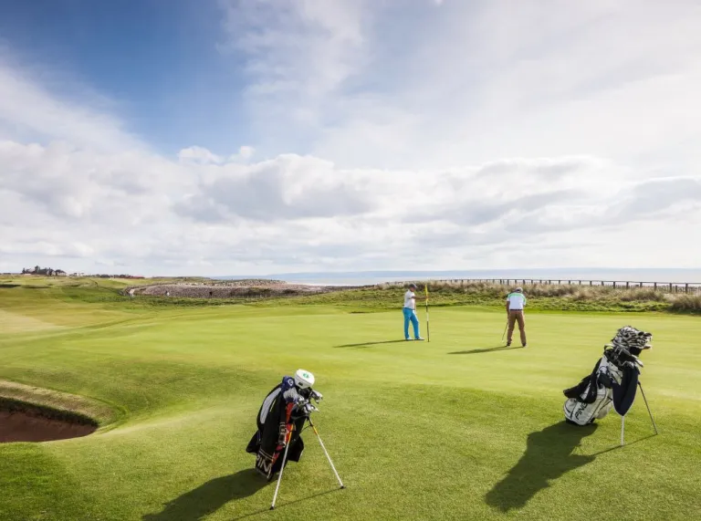 Scène d'extérieur avec des hommes qui jouent au golf sur fond de ciel bleu et de mer.