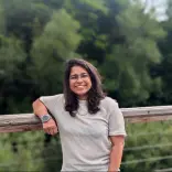 Woman leaning on fence with green foresty in background