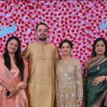 6 people stood in front of pink and red background smiling in Indian clothing