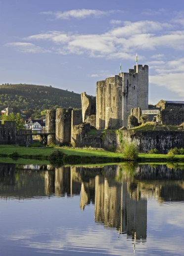 Ruined castle standing by the water in front of a town and surrounding hills.
