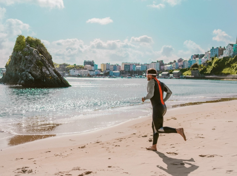Shane Williams, en combinaison, court vers la mer pendant l'entraînement pour le triathlon Ironman Wales sur la Plage Nord de Tenby.