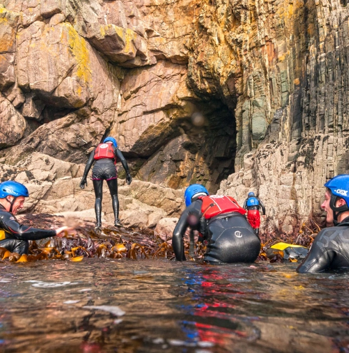 A group of people wearing water safety equipment in the water by the coast
