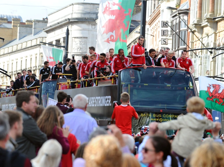 The Wales football team on top of their tour bus waving at crowds below.
