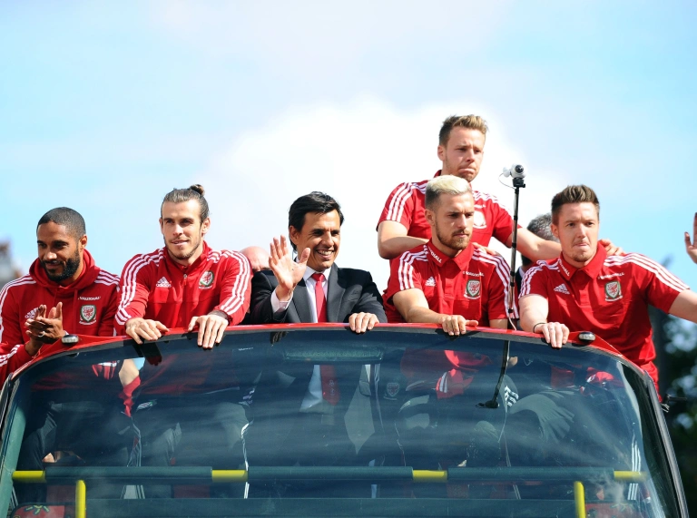 The Wales football team on top of their tour bus waving at crowds below.