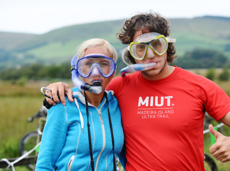 mujer y hombre con el brazo alrededor de ella, ambos tienen snorkels, fondo borroso ladera