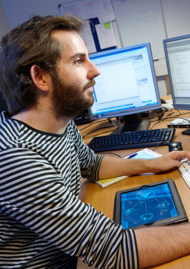 Male employee working at a computer CEMAS - Centre of Excellence in Mobile Applications and Services, University of South Wales