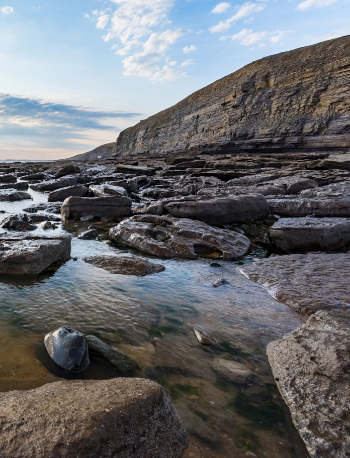 Beach with rocks in the water and steep cliffs in the background.