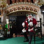 Siôn Corn sitting on a chair by a fire and Christmas decorations.