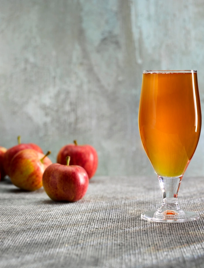 Un vaso de sidra de manzana junto a unas manzanas.