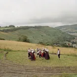 A group of dancers dressed in traditional outfits, dancing on a green hillside with valleys in the distance